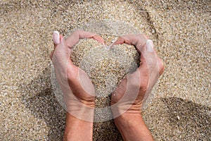 The hands hold the heart - shaped sea sand on the palms . The concept of love, sun, hot summer, relaxing at sea and on the beach.