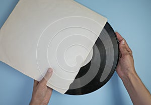 Hands hold an old vinyl record in an old paper case on a light blue background.