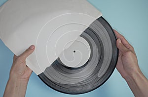 Hands hold an old vinyl record in an old paper case on a light blue background.