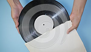 Hands hold an old vinyl record in an old paper case on a light blue background.