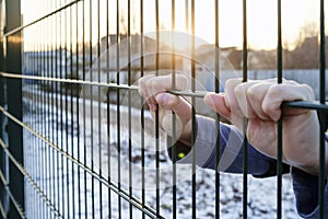 The hands hold onto the metal fence