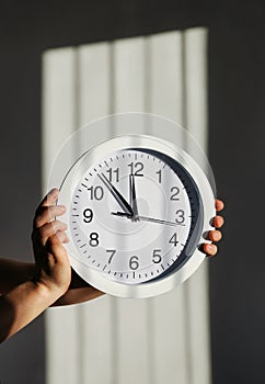 Hands hold round wall clock on background of shadow in form of prison lattice