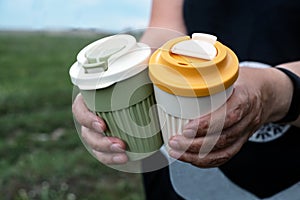 Hands hold two stylish reusable glasses with lids. Zero waste concept