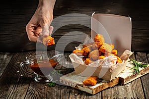 Hands holdin chicken nuggets in ketchup in paper box on a wooden background. American food concept. fast food meal. banner, menu,