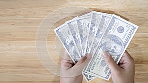 Hands holding 100 dollar bills. Women's hand holds a fan of dollars on wooden table