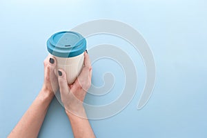 Hands holding bamboo reusable takeaway cup with lid on, on blue background