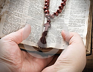 hands holding the Bible and praying with a rosary