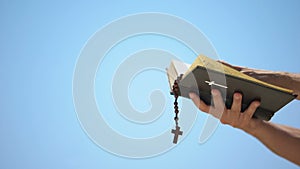 Hands holding bible and rosary on blue background, praying to god, template