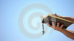 Hands holding bible and rosary on blue background, praying to god, template