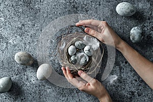 Hands holding bird nest with Easter eggs on blue background. Happy Easter holiday, top view, flat lay
