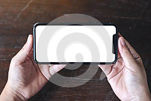 Hands holding black mobile phone with blank desktop screen horizontally on wooden table background