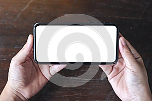 Hands holding black mobile phone with blank desktop screen horizontally on wooden table background