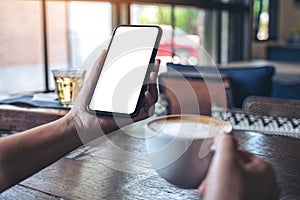 Hands holding black mobile phone with blank screen while drinking coffee in vintage cafe