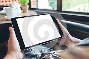 Hands holding black tablet pc with blank white desktop screen while sitting in cafe