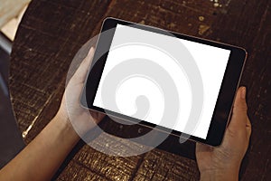 Hands holding black tablet pc with blank white desktop screen on vintage wooden table