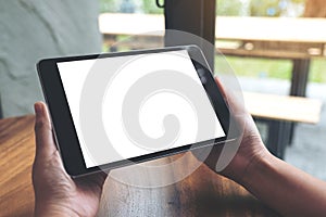 Hands holding black tablet pc with blank white desktop screen on wooden table