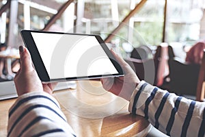 Hands holding black tablet pc with blank white desktop screen on wooden table in cafe