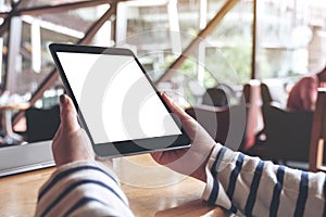 Hands holding black tablet pc with blank white desktop screen on wooden table in cafe