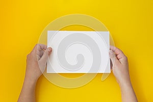 Hands holding blank white, empty paper isolated on yellow with copy space