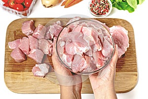 Hands holding a bowl of freshly-cut meat on a wooden cutting board