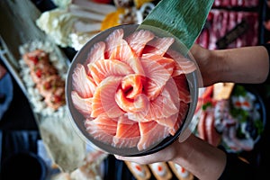 Hands holding a bowl of salmon sashimi