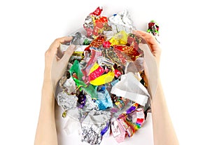 Hands holding a bunch of candy wrappers on a white background. C