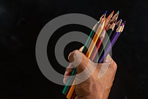 Hands holding a bunch of pencils on a black background