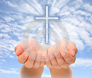 Hands holding Christian cross with light beams