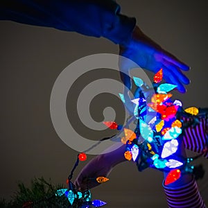 Hands Holding Christmas Lights as They Wrap Them Around a Tree