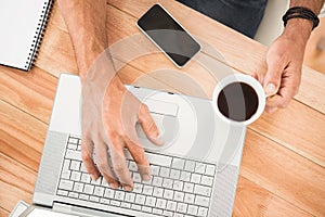 Hands holding coffee cup and typing on laptop