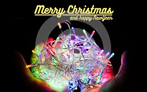 Hands holding colorful wired christmas lights with merry christmas yellow words on top