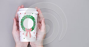 Hands holding craft paper coffee cup, grey background. Christmas or New Year holiday greeting paper coffee cup template. Flat lay