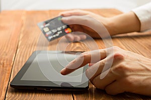 Hands holding credit card typing numbers on tablet pc making online payment at home the wooden table. Online shopping