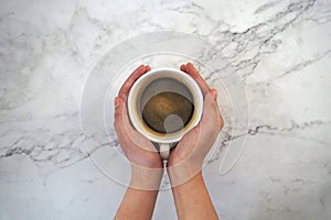 Hands holding a cup of coffee, with marble background