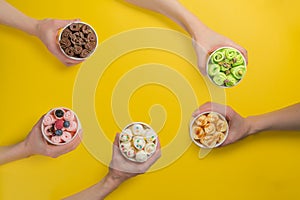 Hands holding cups with different rolled ice cream on bright yellow background