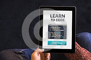 Hands holding tablet with learn to code concept on screen