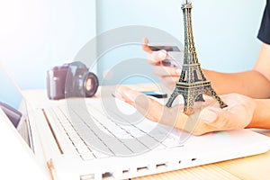 Hands holding eiffel tower model and credit card. Woman using laptop computer and booking hotel. Travel Paris.