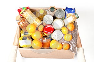 Hands holding food donations box with grocery products on white background. Top view