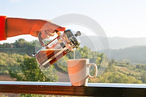 Hands holding french press coffee pot and white cup  with mountain view