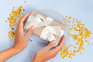 Hands holding a gift against blue background with golden confetti