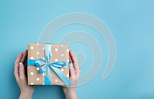 Hands holding a gift box with blue ribbon on light blue background