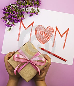 Hands holding a gift box and a mother`s day card for mom, top view. the inscription mother with a big red heart