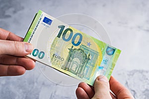 Hands holding and giving one hundred euro banknotes. Stack of money in man hands on gray background