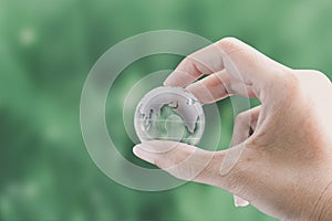 Hands holding globe glass earth with green grass field in side on blurred light nature background. Environment Concept