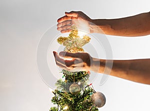 Hands holding golden star on Christmas tree with bright lights, Christmas holiday concept