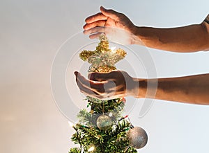 Hands holding golden star on Christmas tree with bright lights, Christmas holiday concept