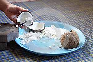 Hands holding a half-cut coconut to scrape for making coconut milk