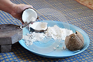 Hands holding a half-cut coconut to scrape for making coconut milk
