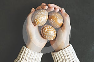 Hands holding hand painted easter eggs on black background, top view shot