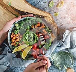 Hands holding healthy superbowl or Buddha bowl with salad, baked sweet potatoes, chickpeas, broccoli, hummus, avocado